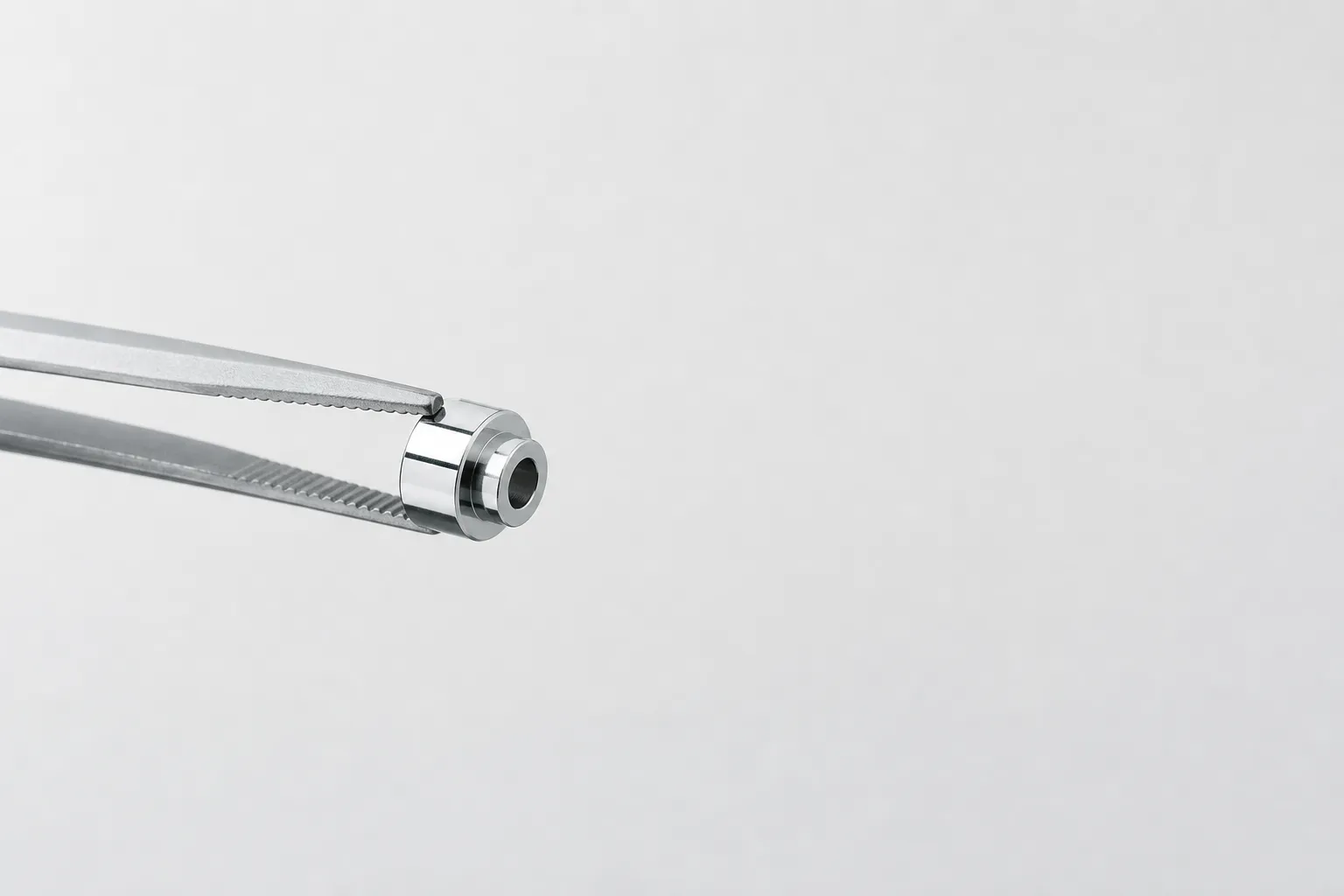 Petite pièce en inox poli miroir tenue par une pince, fond clair et neutre